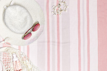 Summer flat lay with sun hat, sunglasses, cosmetics products on striped beach towel as background. Summer holiday, vacation, rest concept. Top view summertime accessories, white pink pastel color fon.