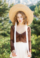 Portrait of sweet blonde girl in straw hat posing on a background of the city.