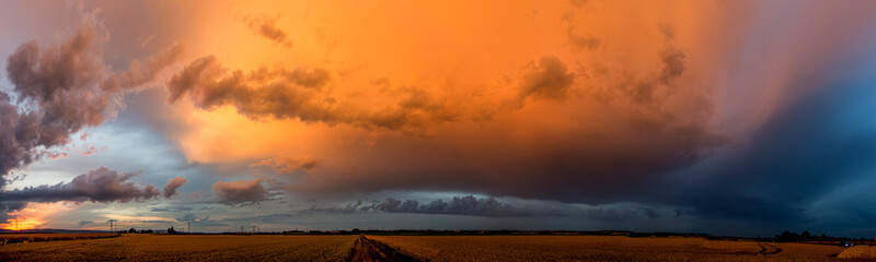 Panoramafoto einer abziehenden Gewitterwolke, die vom Licht der untergehenden Sonne orange...