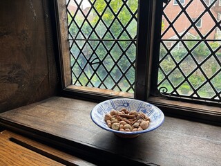 Close up of medieval Elizabethan leaded glass window diamond shape thick hand blown historic glass  light  shadows on ancient historic wood window cill with antique vintage china bowl with tree nuts