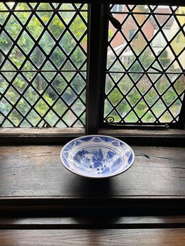 Close up of medieval Elizabethan leaded glass window diamond shape thick hand blown historic glass  light  shadows on ancient historic wood window cill with antique vintage china bowl with tree nuts