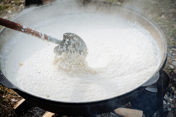 Rice porridge is cooked in a large cauldron on fire, camp kitchen cooking for a large number of...