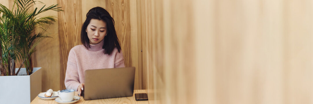 Beautiful asian girl sitting in a laptop in a cafe. Work in a coffee shop. Match and eclair next to a working laptop. Web banner