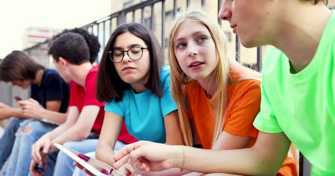 Group of teenagers using digital tablets sitting by railing