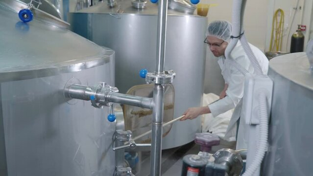 Technician Removes Spent Grain To Clean Beer Brewing Tank Equipment. Extracting Spent Grain From Reservoir Of Ale Production Equipment. Brewery Equipment. Spent Grain Waste. Worker In Sterile Uniform