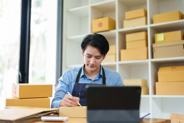 small startup, and SME owner, an Asian male entrepreneur, is writing down information on a notepad to organize the product before packing it into the inner box for the customer