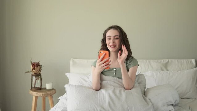 Beautiful young woman sitting in bed having video call on smartphone