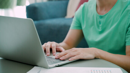 Close-up of a young Asian man's hand, resting on his laptop computer, and the other hand clutching...