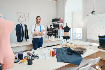Man couturier stands among sewing equipment with arms crossed on chest