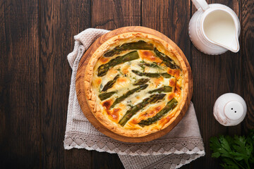 Quiche. Homemade asparagus pie or quiche with cheese and spinach on old dark wooden table background. Top view.