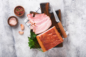 Whole Smoked Slab Bacon. Brisket. Sliced smoked gammon on a wooden table with rosemary, parsley,...