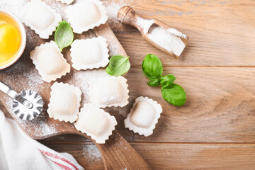 Ravioli Italian food. Tasty homemade pasta ravioli with flour, tomatoes, eggs and greens basil on wooden background. Process of making italian ravioli. Food cooking ingredients background. Top view.