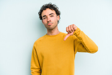 Young caucasian man isolated on blue background showing a dislike gesture, thumbs down....