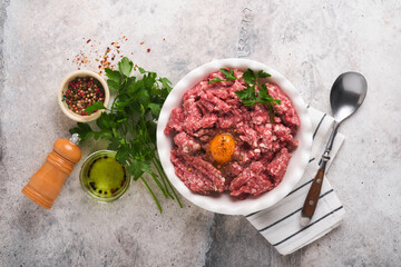 Raw minced meat. Ground meat beef, pork or lamb spices, herbs and eggs on white plate on light grey...