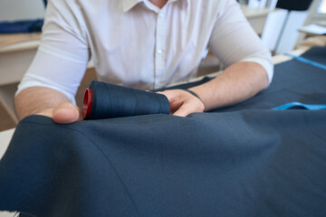 Man couturier picks threads under piece of black fabric