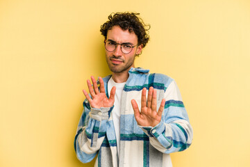 Young caucasian man isolated on yellow background rejecting someone showing a gesture of disgust.