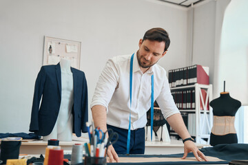 Couturier in sewing workshop applies a pattern to black fabric