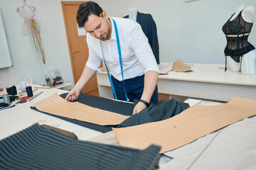 Man couturier applies pattern on black fabric in sewing workshop