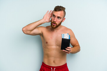 Fototapeta premium Young caucasian man holding a passport isolated on blue background trying to listening a gossip.