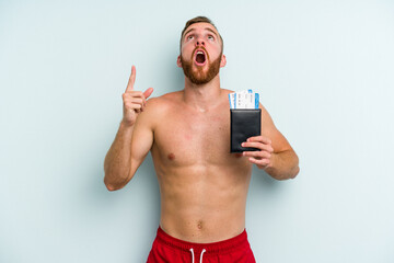 Young caucasian man holding a passport isolated on blue background pointing upside with opened mouth.