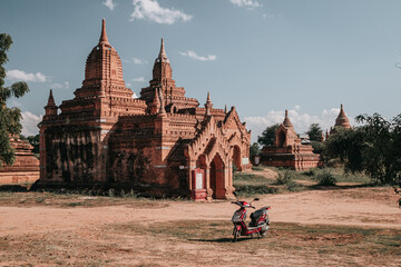 Buddhist temple in the ancient city of Bagan, Myanmar on a sunny day with a motorbike parked in front of the temple - obrazy, fototapety, plakaty