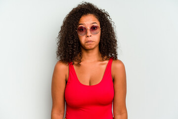Young brazilian woman wearing a swimsuit isolated on blue background shrugs shoulders and open eyes...