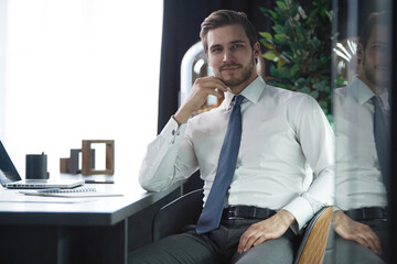 Portrait of businessman sitting in office, successful man worker employee by work desk looking at camera