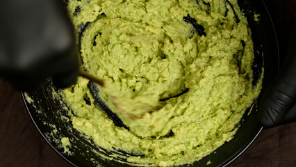 Hands mashing avocado in a black bowl with fork. Making guacamole sauce mashing avocado