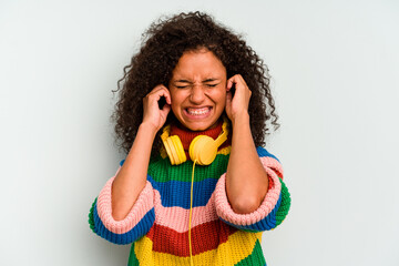 Young Brazilian woman listening to music isolated on blue background covering ears with hands.
