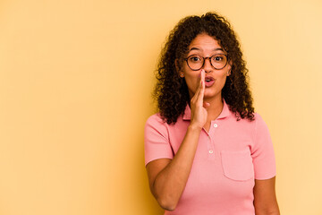 Young Brazilian woman isolated on yellow background is saying a secret hot braking news and looking...
