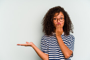 Young Brazilian woman isolated on blue background impressed holding copy space on palm.