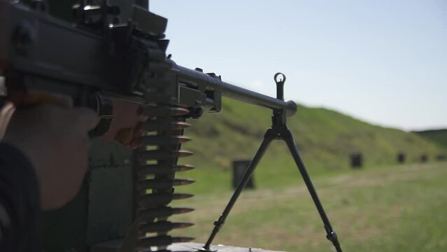 Militarian sets loaded machine gun with cartridge belt on bipod and ready to shot at shooting range