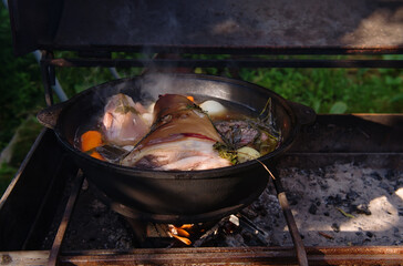 Ready pork knuckle in beer, in a pot after four hours of cooking on an open wood fire. With tomatoes, beef, onions, garlic, celery and carrots. the concept of a weekend in nature