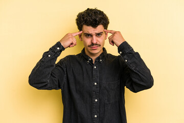 Young caucasian man isolated on yellow background focused on a task, keeping forefingers pointing head.