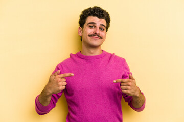 Young caucasian man isolated on yellow background person pointing by hand to a shirt copy space, proud and confident