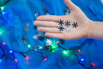 Female hand holds five silver snowflakes on the blue background with the colorful garland. Winter, New Year concept
