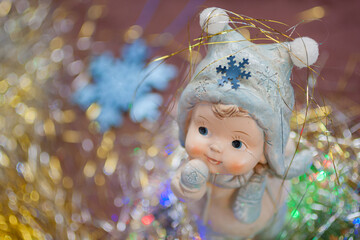 Top view of the ceramic figure of a cute little child in the winter clothes with the glittering snowflake and the golden tinsel on his cap. New year, Christmas background with the space for text