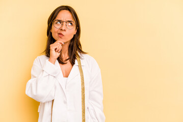 Young nutritionist hispanic woman isolated on yellow background looking sideways with doubtful and...