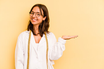Young nutritionist hispanic woman isolated on yellow background showing a copy space on a palm and...