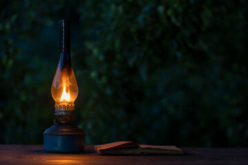 Old antique burning kerosene lamp with open book on the wooden table, copy space