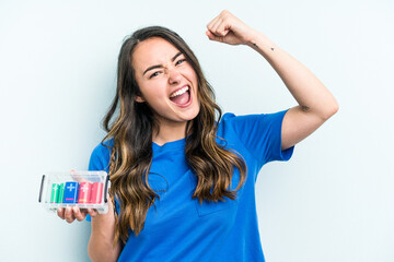 Young caucasian woman holding batteries isolated on blue background raising fist after a victory, winner concept.