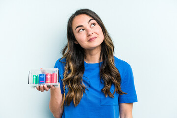 Young caucasian woman holding batteries isolated on blue background dreaming of achieving goals and purposes