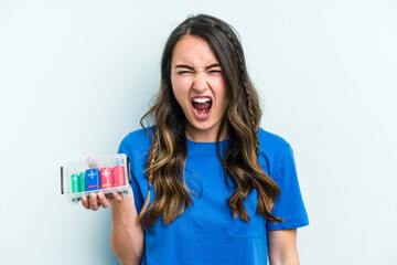 Young caucasian woman holding batteries isolated on blue background screaming very angry and aggressive.