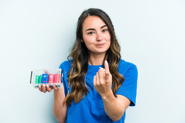 Young caucasian woman holding batteries isolated on blue background pointing with finger at you as if inviting come closer.