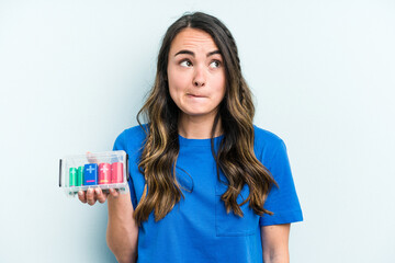 Young caucasian woman holding batteries isolated on blue background confused, feels doubtful and unsure.