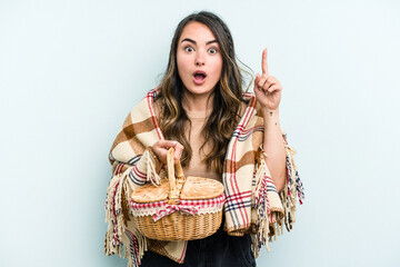Young caucasian woman holding a picnic basket isolated on blue background having an idea, inspiration concept.