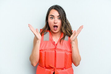 Young caucasian woman wearing life jacket isolated on blue background surprised and shocked.