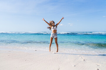 Carefree female jumping at seashore beach - enjoying summer freedom on getaway vacations for...