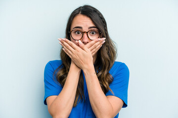 Young caucasian woman isolated on blue background covering mouth with hands looking worried.