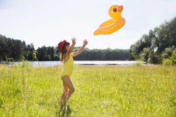 child girl in swimming suit with Duck shaped inflatable ring goes to swim on the lake during the...